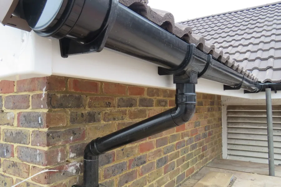 Black gutter and downpipe running along the eaves of a brick house